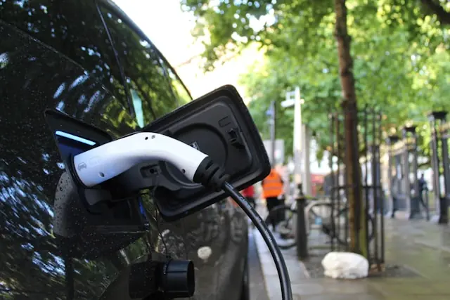 Weißer Typ-2-Ladestecker in der Ladebuchse eines schwarzen Elektroautos auf einer belebten Stadtstraße, im Kontext des Börsengangs von Aptera Motors.
