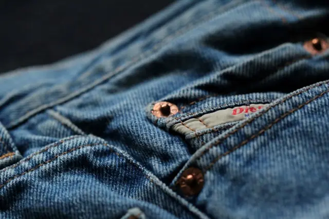 Nahaufnahme einer blauen Jeans mit Kupfernieten, Knopfleiste und rotem Markenetikett vor dem Hintergrund der Preise für Vintage-Jeans