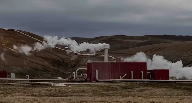 Rotes Geothermiekraftwerk mit Dampfsäulen und Rohrleitungen vor Hügeln, im Zusammenhang mit dem Fervo-Börsengang an der Nasdaq