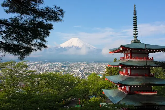 Japanische Pagode mit Blick auf eine Stadt und den schneebedeckten Fuji als Hintergrundbild zum Börsenaufschwung in Japan.