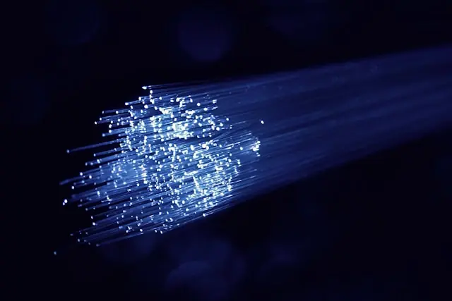 Ein Bündel leuchtender Glasfaserkabel strahlt blaues Licht vor dunklem Hintergrund aus und steht für moderne Netzwerktechnik.