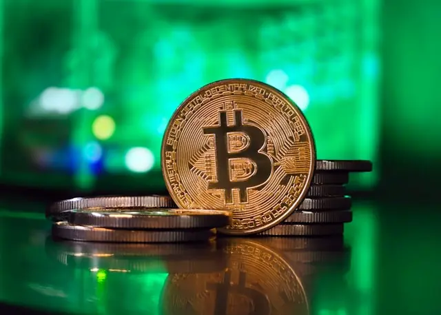 Goldfarbene Bitcoin-Münze aufrecht vor gestapelten Münzen und grün beleuchtetem Hintergrund als Bezug zum Kurssprung der MARA-Aktie und Bitcoin über 72.000 Dollar