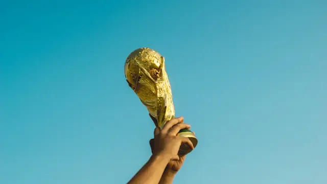Hand hält einen goldenen WM-Pokal vor blauem Himmel als Bezug zur Fußball-WM 2026 und ihrer Wirkung auf Aktienkurse