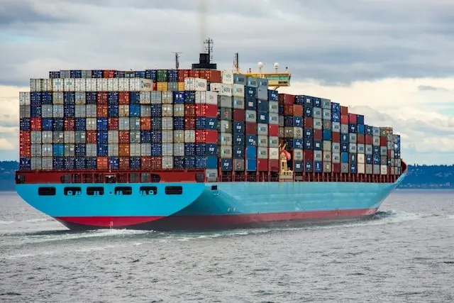Beladenes Containerschiff mit blauem Rumpf und bunten Containerstapeln auf offener See als Bezug zur Schiffsortung per Funksignal-Satelliten
