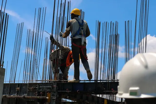 Bauarbeiter mit gelbem Helm und Sicherheitsgurt zwischen Bewehrungsstahl vor blauem Himmel, im Kontext des SOLV-Energy-Börsengangs