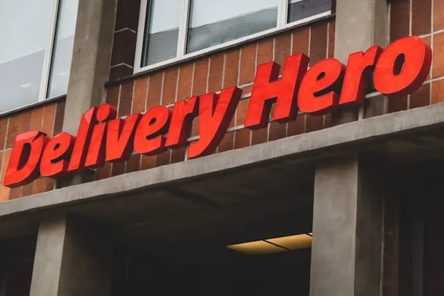 Roter Delivery-Hero-Schriftzug in 3D-Buchstaben an einer Backsteinfassade als Bezug zum Übernahmeangebot von Uber