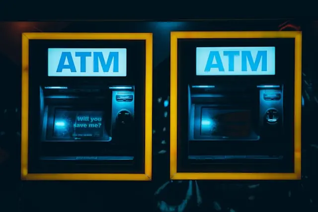 Zwei beleuchtete Geldautomaten mit gelben Rahmen bei Nacht, ein Display ruft zum Sparen auf – Bezug zur UmweltBank-Kapitalerhöhung