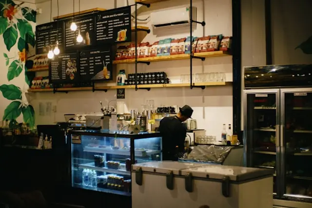Barista arbeitet hinter der Theke einer Kaffeebar mit beleuchteten Menütafeln, passend zum geplanten Börsengang von Black Rock Coffee Bar