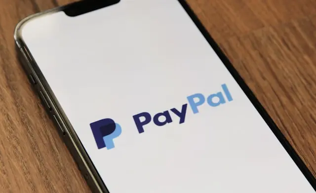 PayPal-Logo auf dem Display eines Smartphones auf einem Holztisch als Bezug zum Übernahmeangebot von Stripe und Advent