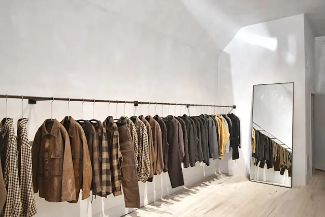 Jacken und Mäntel auf einer Kleiderstange in einem minimalistischen Showroom, im Hintergrund ein Standspiegel – im Kontext des Kurseinbruchs bei PVH nach Prognosesenkung.