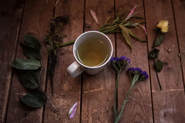 Eine weiße Tasse Kräutertee steht auf einem dunklen Holztisch, umgeben von getrockneten Blüten und Blättern – im Kontext des Börsengangs des chinesischen Teeketten-Konzepts Chagee.