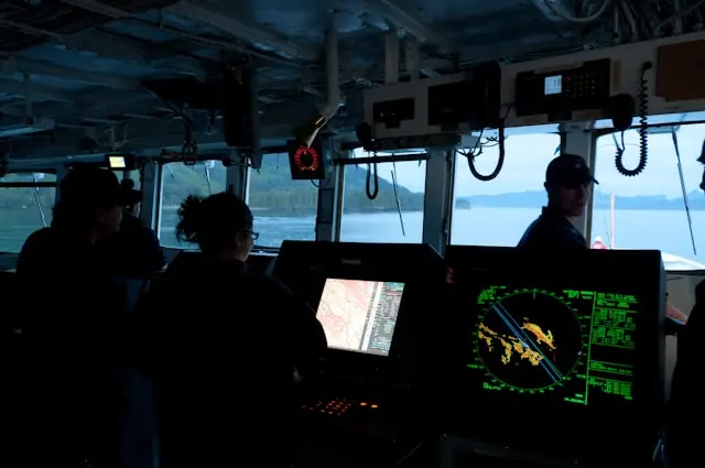 Dunkle Kommandobrücke eines Schiffs mit Radar- und Kartenbildschirmen sowie Besatzung vor Fenstern zum Wasser, im Kontext von HawkEye 360.