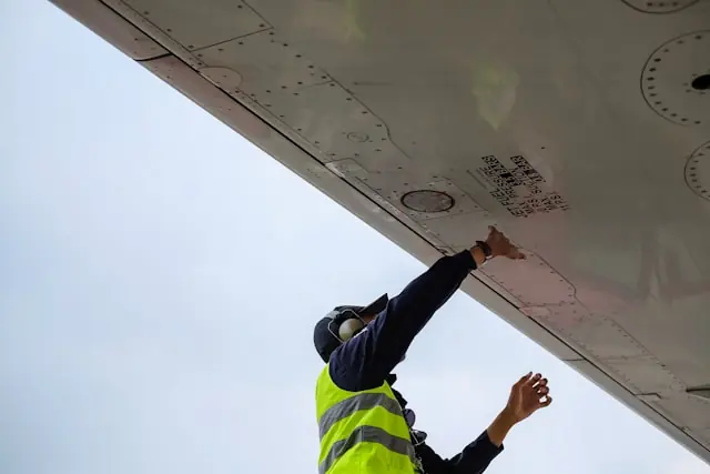 Techniker in Warnweste inspiziert von unten die Flügelunterseite eines Flugzeugs im Zusammenhang mit dem Nasdaq-Listing von Odysight.ai
