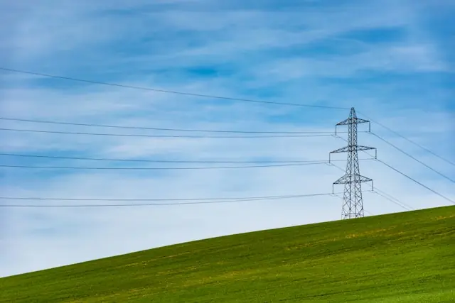 Strommast mit Hochspannungsleitungen über grünem Hügel unter blauem Himmel als Bezug zur Kurserholung von Edison International