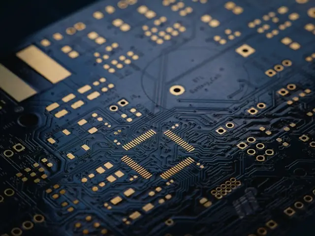 Nahaufnahme einer blauen Leiterplatte mit goldenen Leiterbahnen und Chips als Bezug zum Kursrückgang bei Broadcom trotz Rekordergebnissen.
