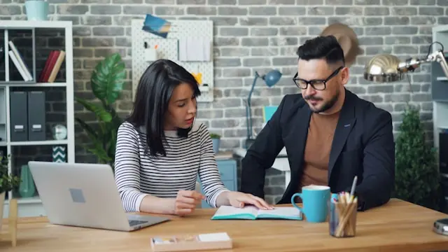 Zwei Kollegen sitzen an einem Schreibtisch mit Laptop und Notizbuch, im Kontext des Nasdaq-Börsengangs von Ethos Technologies.