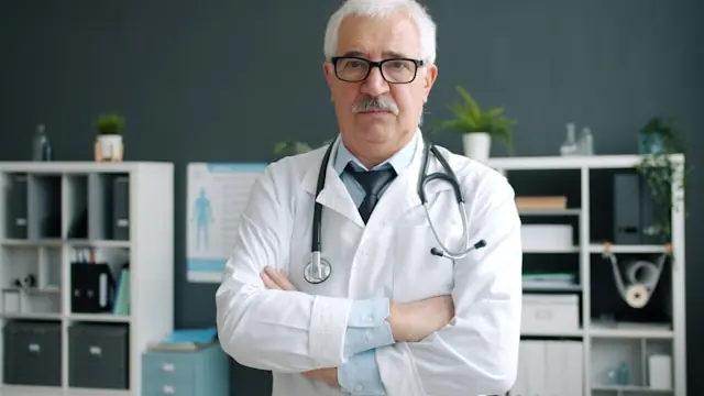 Älterer Arzt mit weißem Haar, Brille und Stethoskop mit verschränkten Armen in einer Praxis, Bezug zum Börsengang von Omada Health