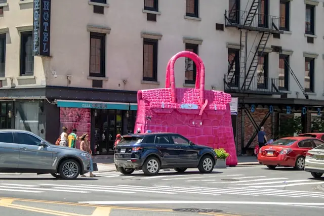 Überdimensionale pinke Handtaschen-Installation vor einer Häuserfassade mit Straßenverkehr im Zusammenhang mit der Zuteilungspraxis bei Birkin-Taschen